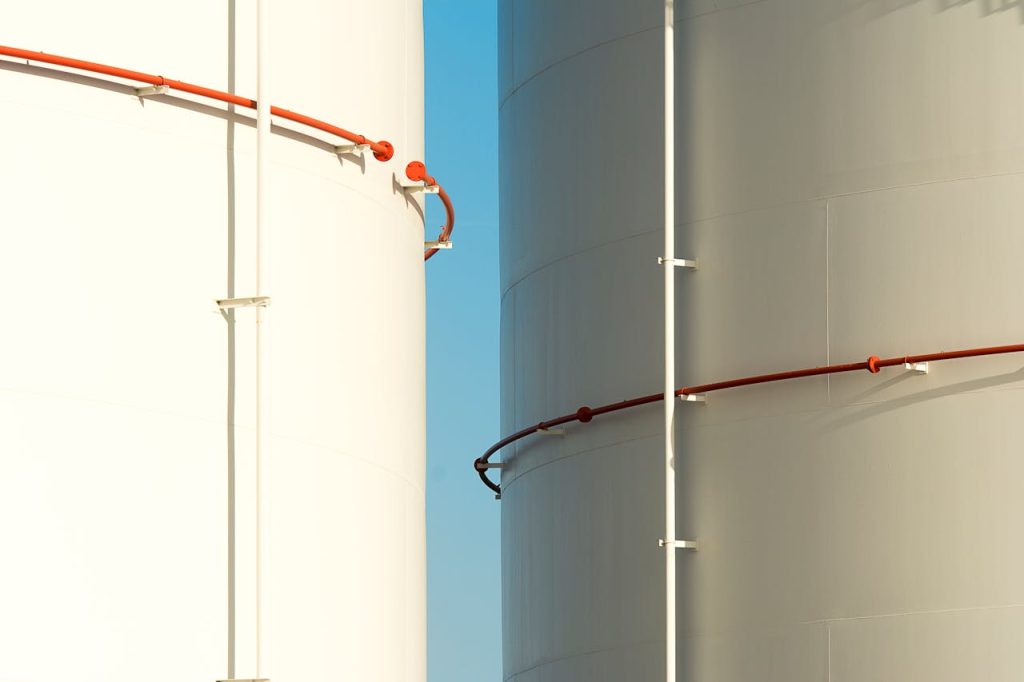 Close-up of two industrial silos with piping against a clear blue sky.