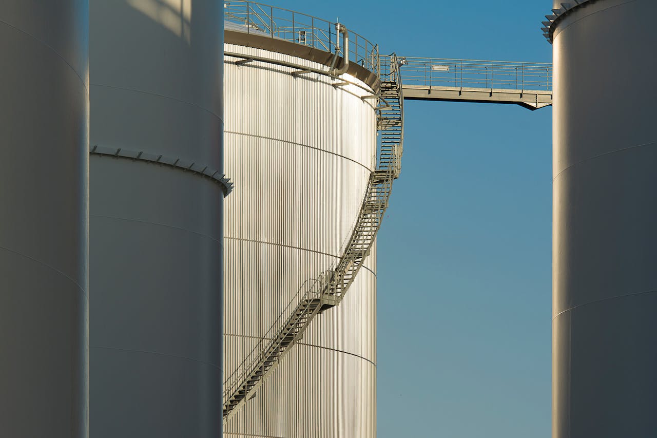 Close-up view of metal industrial silos with a connecting staircase against a clear blue sky.